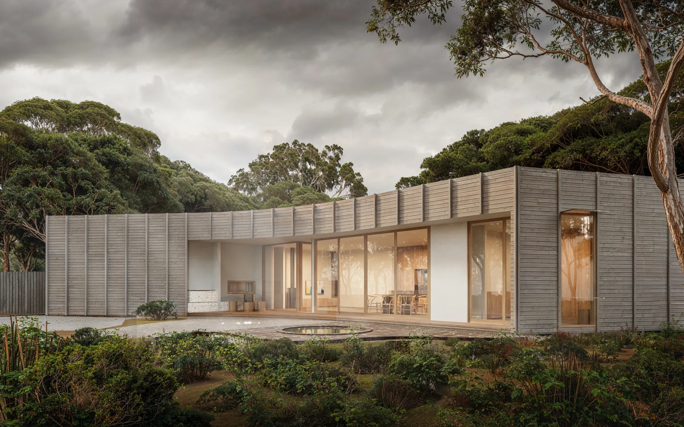 Low contemporary forest house with restrained timber cladding, warm glazing and mature trees